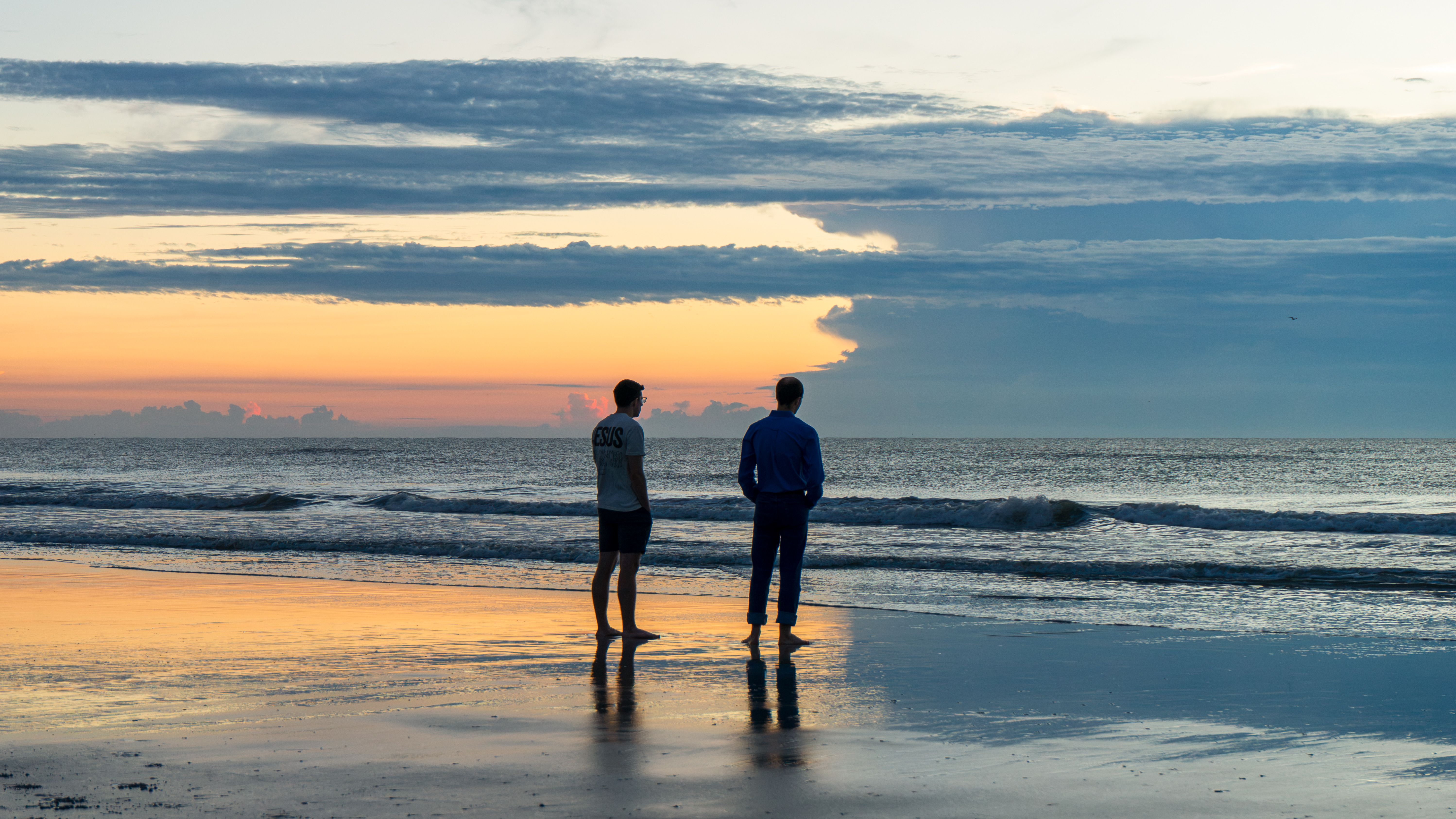 Two people on the shoreline at sunrise