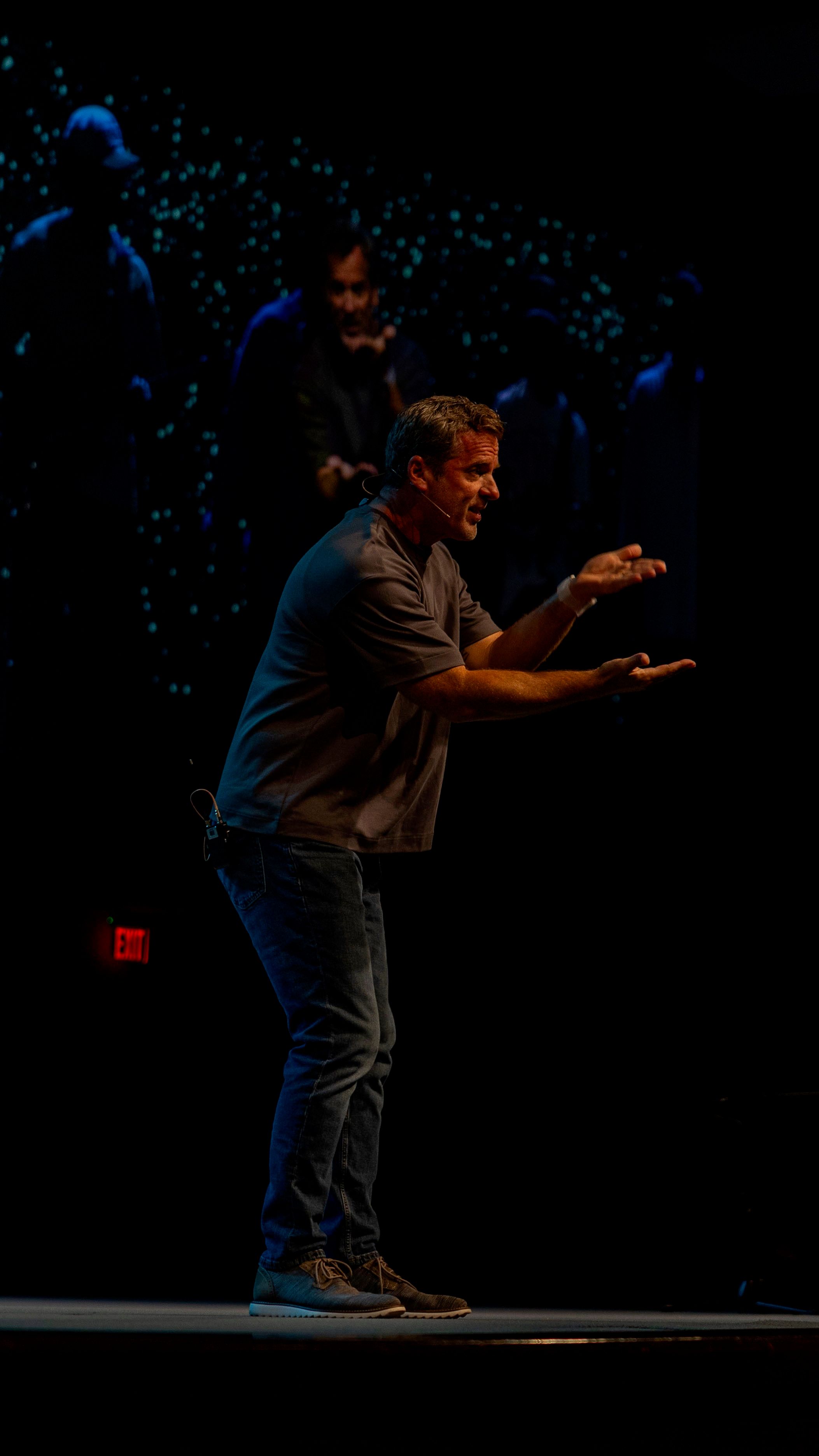 Speaker mid-gesture on a dark stage