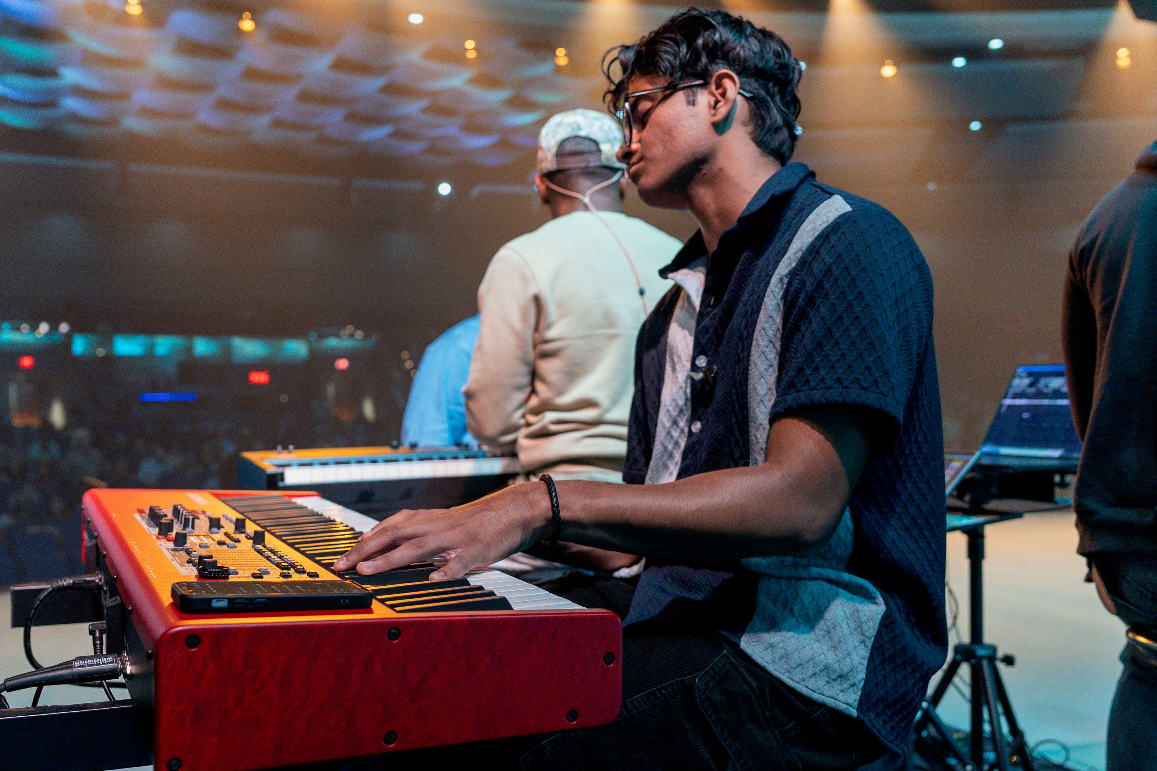 Keyboardist leaning into a red keyboard on stage, lit warm from above
